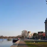 Ein sonniger Tag am Wasser in Potsdam. Ein Mann liest im Gras, ein Fahrrad steht daneben. Im Hintergrund ein Turm und moderne Gebäude.