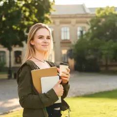 Junge Frau mit Büchern und Kaffee vor einem Universitätsgebäude. Sie denkt darüber nach, wie lange dauert ein Masterstudium.
