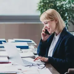 Eine Frau am Telefon und Laptop, die sich mit dem Steuerrecht beschäftigt.