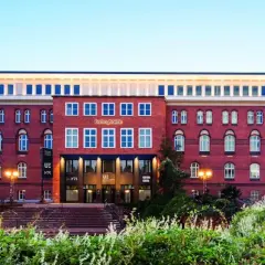Das Gebäude der University of Europe Hamburg, ein roter Backsteinbau mit vielen Fenstern, umgeben von Grün.