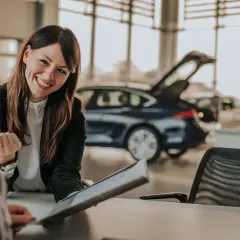 Lächelnde Automobilkauffrau erklärt Unterlagen. Die Ausbildung zur Automobilkauffrau bietet gute Perspektiven, auch beim Gehalt.