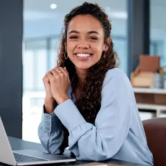 Lächelnde junge Frau am Schreibtisch mit Laptop. Sie informiert sich über den industriekaufmann verdienst ausbildung.