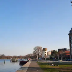 Ein sonniger Tag am Wasser in Potsdam. Ein Mann liest im Gras, ein Fahrrad steht daneben. Im Hintergrund ein Turm und moderne Gebäude.