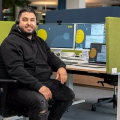 Ein Mann mit Headset sitzt am Schreibtisch, umgeben von Monitoren. Er ist ein Kaufmann im Dialogmarketing, dessen Gehalt hier thematisiert wird.