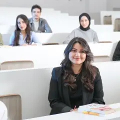 Junge Frau im Anzug in einem Hörsaal, umgeben von Kommilitonen. Sie lernt, um **Anwalt zu werden ohne Abitur**.