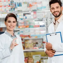 Zwei freundliche Apotheker in weißen Kitteln, die Medikamente und eine Patientenakte präsentieren. Einblick in verschiedene Berufe auf Deutsch.