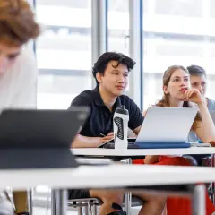 Studenten im Hörsaal, die sich auf ihre Lektionen konzentrieren. Ein junger Mann mit einem schwarzen Poloshirt und einer Wasserflasche, der aufmerksam zuhört. Dies ist ein typisches Bild für Management and Technology TUM.