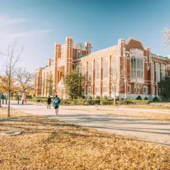 Herbstliche Szene auf einem Campus in den USA, mit Studenten, die an einem Backsteingebäude vorbeigehen. Ein schöner **college usa vergleich deutschland**-Moment.
