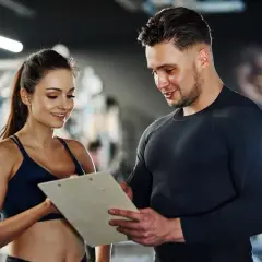 Ein Trainer bespricht mit einer Kundin Trainingspläne. Das Gehalt eines Sport- und Fitnesskaufmanns nach der Ausbildung ist attraktiv.