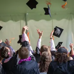 Absolventen werfen ihre Hüte in die Luft. Ein junger Mann feiert seinen Abschluss als Bachelor Ingenieur.