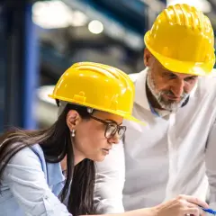 Zwei Ingenieure in gelben Helmen besprechen Pläne am Laptop. Sie arbeiten an einem Projekt, um Ingenieur zu werden.