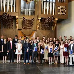 Absolventen mit Urkunden vor einer Orgel, die ihr erfolgreiches Diplom Studium feiern.