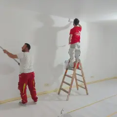 Zwei Maler streichen Wände und Decke weiß. Die Ausbildung zum Maler und Lackierer bietet ein gutes Gehalt netto.