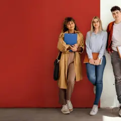Vier Studierende der ham hochschule lehnen entspannt an einer Wand, Bücher und Hefte in den Händen.