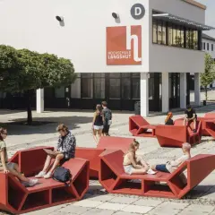 Studierende entspannen auf roten Sitzmöbeln vor der Hochschule Landshut.
