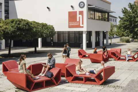 Studierende entspannen auf roten Sitzmöbeln vor der Hochschule Landshut.