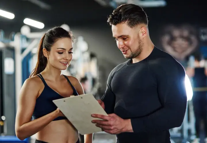 Ein Trainer bespricht mit einer Kundin Trainingspläne. Das Gehalt eines Sport- und Fitnesskaufmanns nach der Ausbildung ist attraktiv.