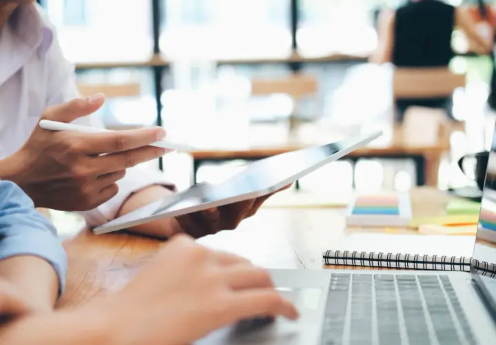 Zwei Personen arbeiten an einem Laptop und Tablet. Sie studieren für ihren **bachelor in business administration**.