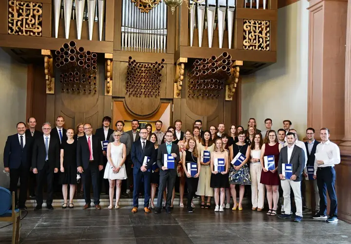 Absolventen mit Urkunden vor einer Orgel, die ihr erfolgreiches Diplom Studium feiern.