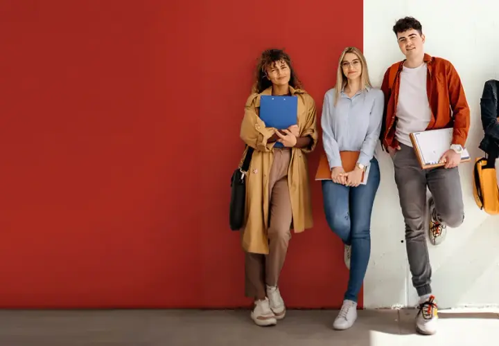 Vier Studierende der ham hochschule lehnen entspannt an einer Wand, Bücher und Hefte in den Händen.