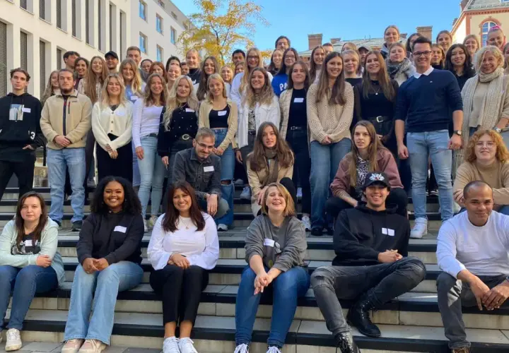 Eine Gruppe junger Leute posiert lächelnd vor einem Gebäude der HS Fresenius Hamburg.