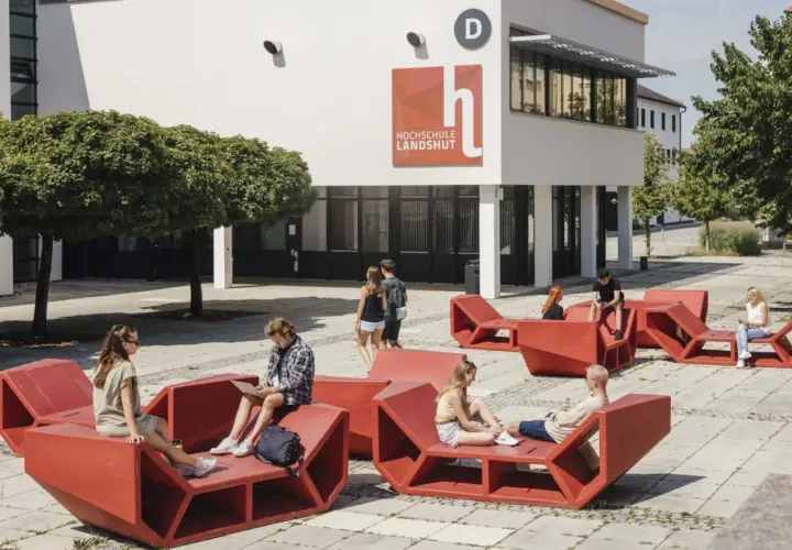 Studierende entspannen auf roten Sitzmöbeln vor der Hochschule Landshut.