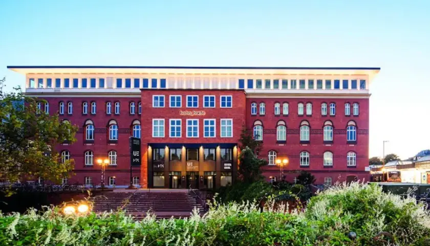 Das Gebäude der University of Europe Hamburg, ein roter Backsteinbau mit vielen Fenstern, umgeben von Grün.