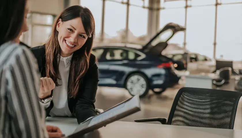 Lächelnde Automobilkauffrau erklärt Unterlagen. Die Ausbildung zur Automobilkauffrau bietet gute Perspektiven, auch beim Gehalt.