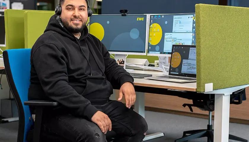 Ein Mann mit Headset sitzt am Schreibtisch, umgeben von Monitoren. Er ist ein Kaufmann im Dialogmarketing, dessen Gehalt hier thematisiert wird.