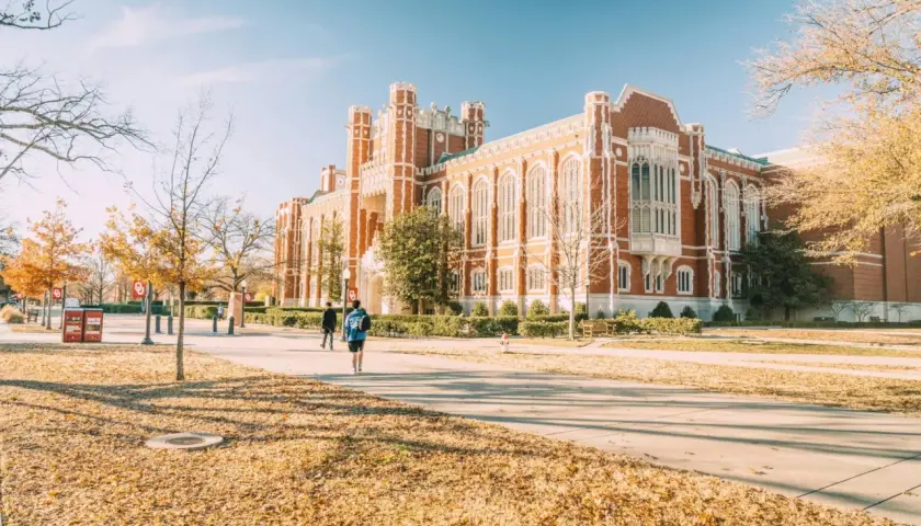 Herbstliche Szene auf einem Campus in den USA, mit Studenten, die an einem Backsteingebäude vorbeigehen. Ein schöner **college usa vergleich deutschland**-Moment.