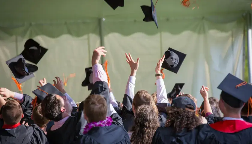 Absolventen werfen ihre Hüte in die Luft. Ein junger Mann feiert seinen Abschluss als Bachelor Ingenieur.