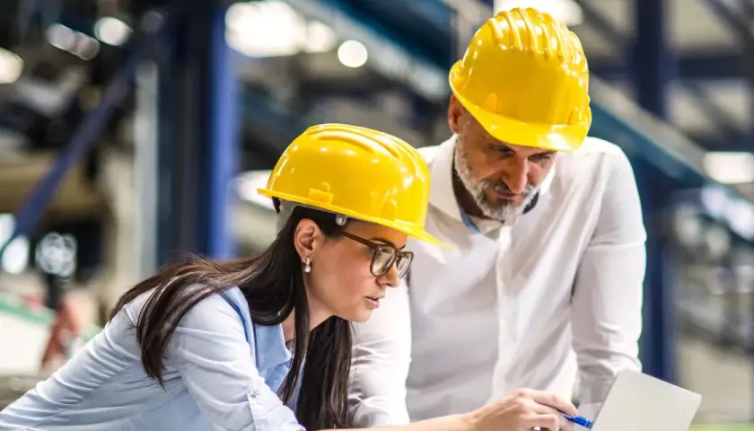Zwei Ingenieure in gelben Helmen besprechen Pläne am Laptop. Sie arbeiten an einem Projekt, um Ingenieur zu werden.