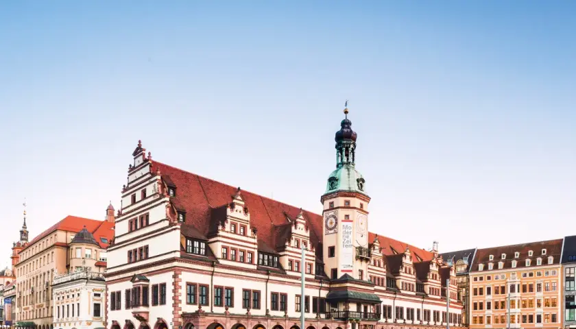 Altes Rathaus mit Turm und moderner Architektur in Leipzig. Die Fassade des Rathauses ist mit roten Ziegeln und weißen Verzierungen geschmückt.