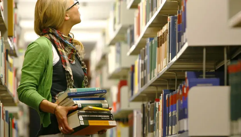 Studentin mit Büchern in der Bibliothek, vielleicht auf dem Weg zu ihrem **hiwi job**.