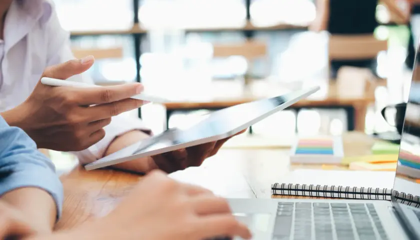 Zwei Personen arbeiten an einem Laptop und Tablet. Sie studieren für ihren **bachelor in business administration**.