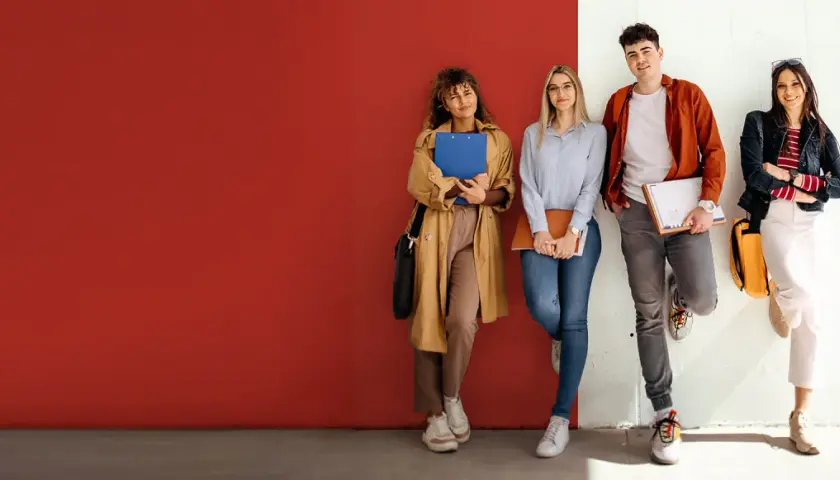 Vier Studierende der ham hochschule lehnen entspannt an einer Wand, Bücher und Hefte in den Händen.