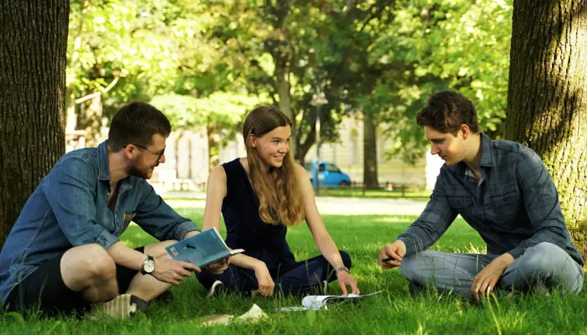 Drei Studierende diskutieren im Grünen über Umweltethik an der Uni Augsburg.