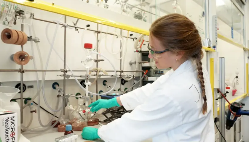 Junge Frau im Labor mit Schutzbrille und Handschuhen, die an einem Experiment arbeitet. Ein Schritt auf dem Weg zum Promotion Studium.