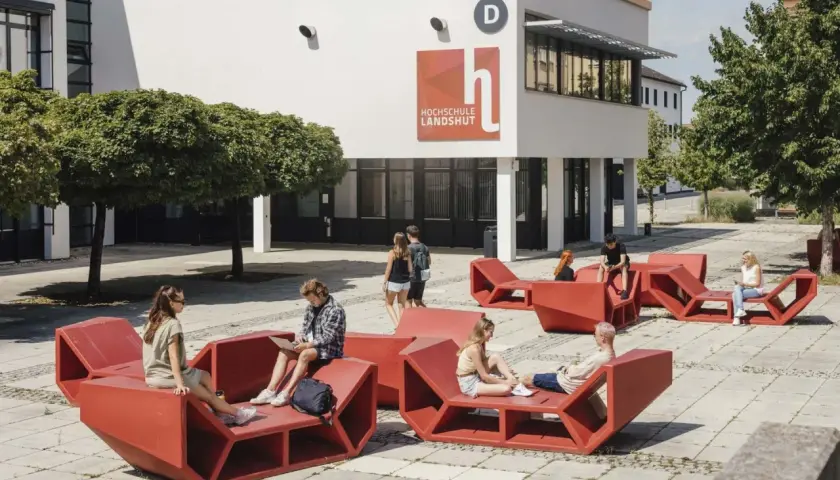 Studierende entspannen auf roten Sitzmöbeln vor der Hochschule Landshut.