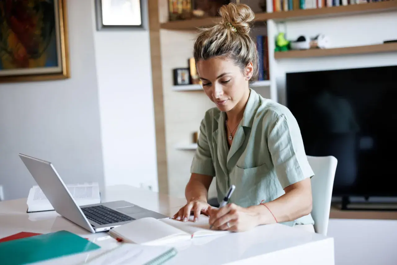 Junge Frau schreibt Notizen, während sie am Laptop arbeitet. Sie plant ihre nächsten Schritte, um ihren Dolmetscher Verdienst zu steigern.