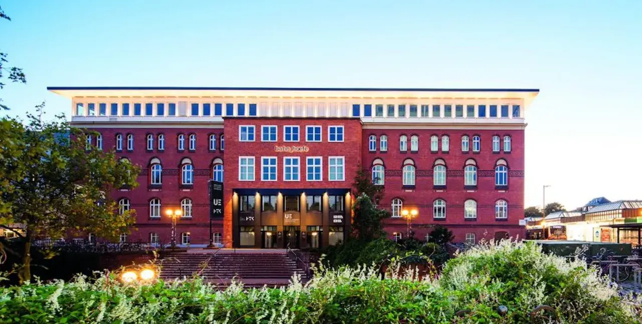 Das Gebäude der University of Europe Hamburg, ein roter Backsteinbau mit vielen Fenstern, umgeben von Grün.