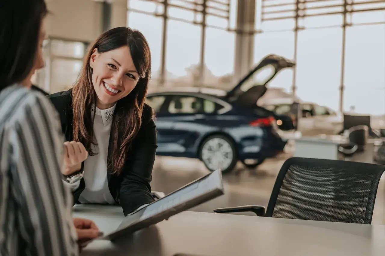 Lächelnde Automobilkauffrau erklärt Unterlagen. Die Ausbildung zur Automobilkauffrau bietet gute Perspektiven, auch beim Gehalt.