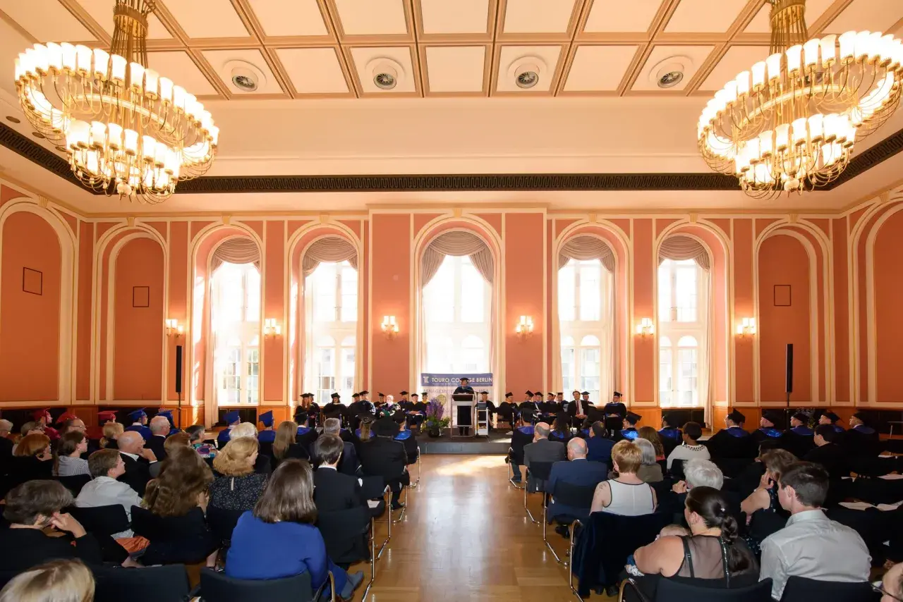 Absolventen der Touro University Berlin feiern ihren Abschluss in einem prunkvollen Saal mit Kronleuchtern.