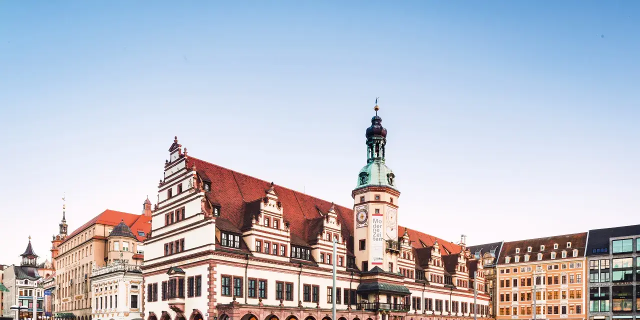Altes Rathaus mit Turm und moderner Architektur in Leipzig. Die Fassade des Rathauses ist mit roten Ziegeln und weißen Verzierungen geschmückt.
