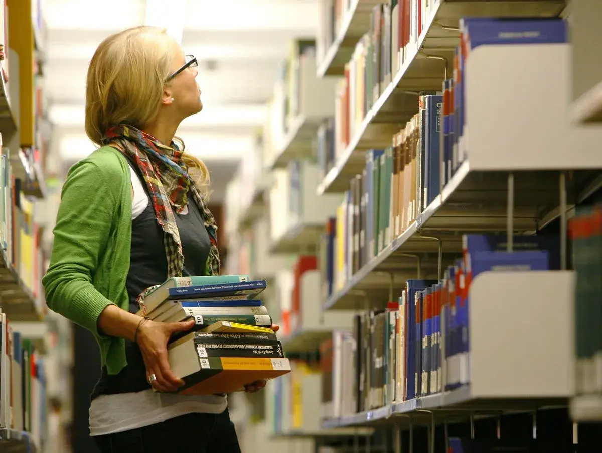 Studentin mit Büchern in der Bibliothek, vielleicht auf dem Weg zu ihrem **hiwi job**.