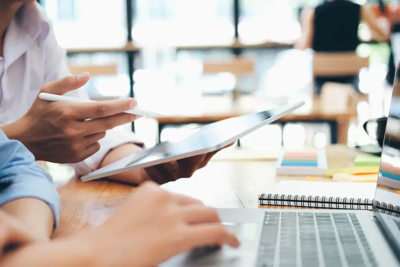 Zwei Personen arbeiten an einem Laptop und Tablet. Sie studieren für ihren **bachelor in business administration**.