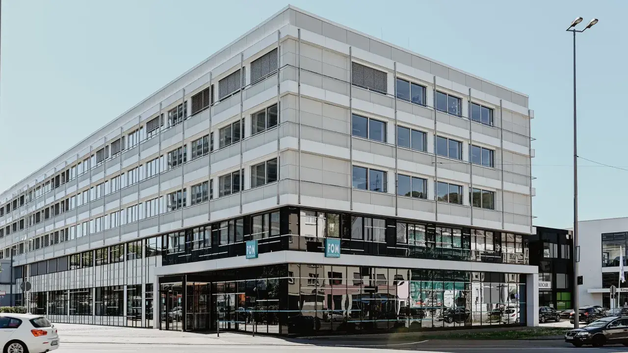 Modernes Gebäude der FOM Hochschule in Wuppertal. Helle Fassade mit vielen Fenstern, unten dunkle Glasfront.