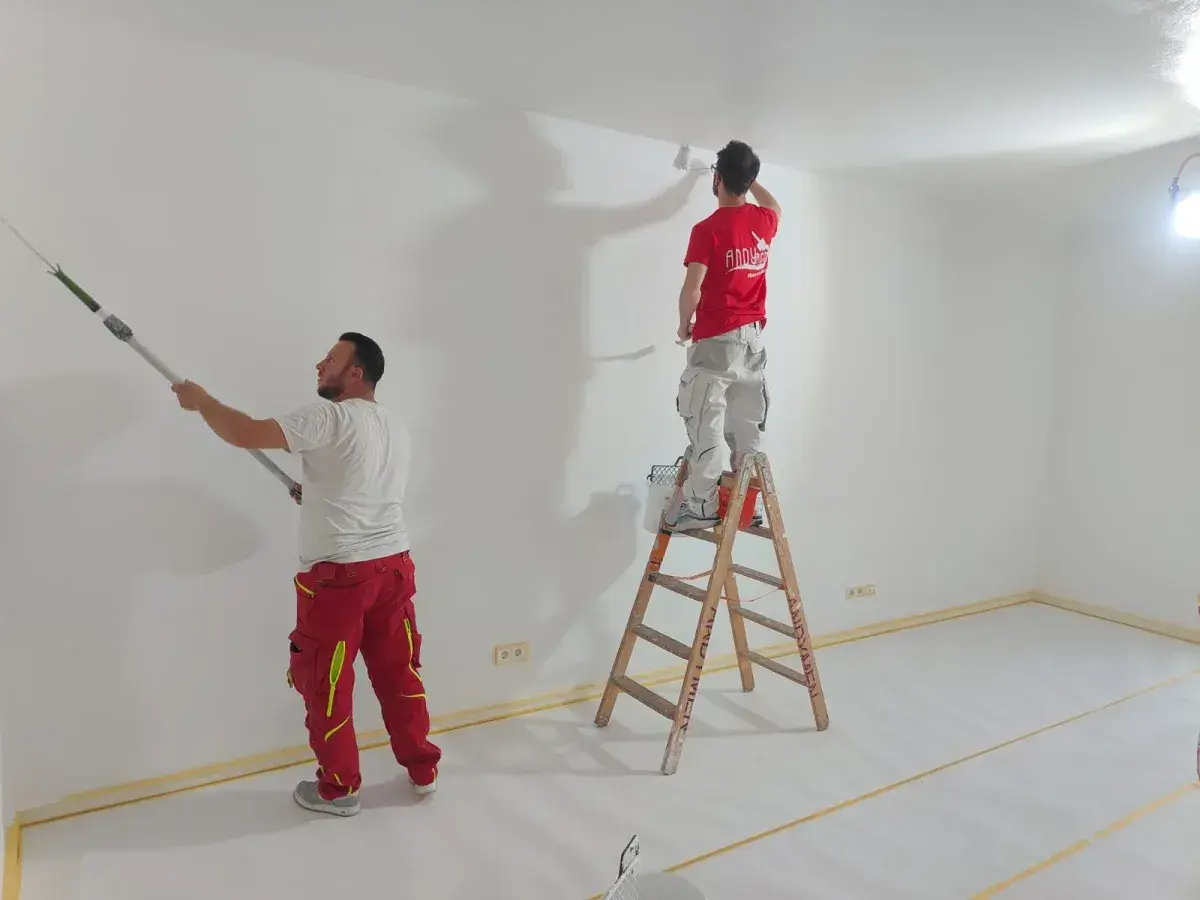 Zwei Maler streichen Wände und Decke weiß. Die Ausbildung zum Maler und Lackierer bietet ein gutes Gehalt netto.
