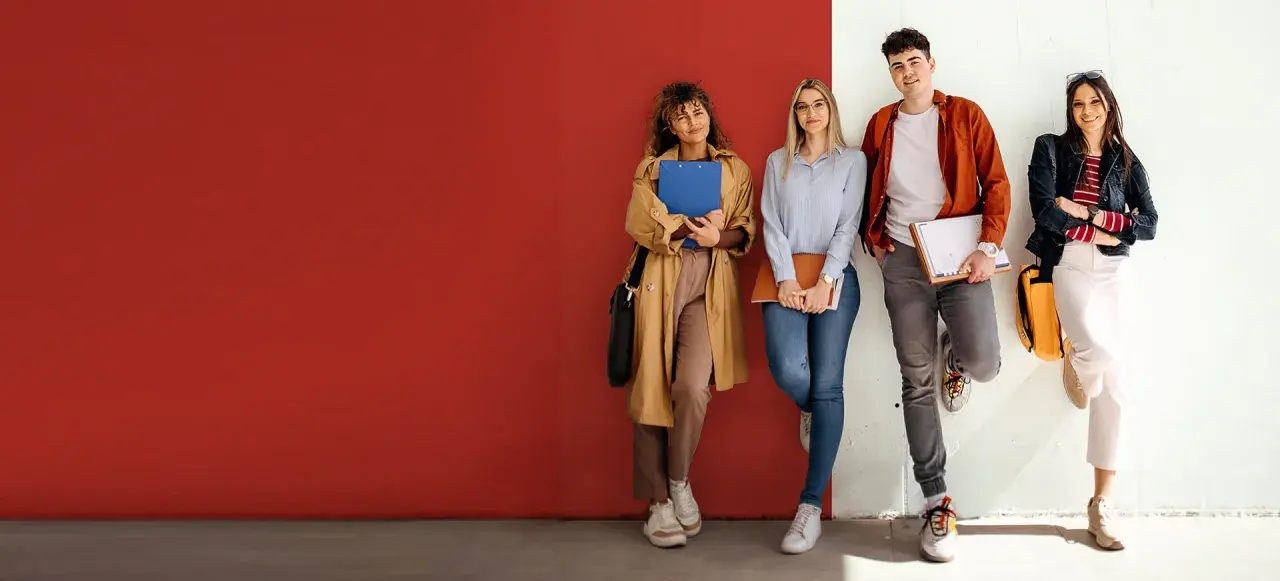 Vier Studierende der ham hochschule lehnen entspannt an einer Wand, Bücher und Hefte in den Händen.