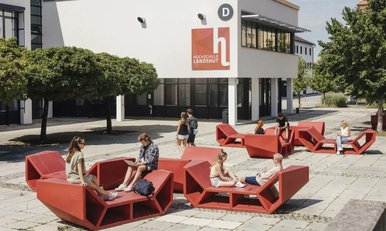 Studierende entspannen auf roten Sitzmöbeln vor der Hochschule Landshut.